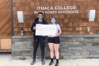 people holding a big check in front of a boathouse