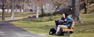 2 students having a discussion on a park bench with laptops out