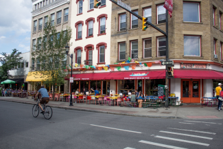 This is a photo of downtown Ithaca, the street corner of Viva restaurant and the Alehouse. There is a white crosswalk and a person riding a bike.