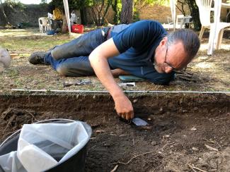 Dr Stull laying down to excavate a feature in an archaeological unit