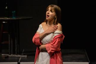 A solo opera singer with her hand on her chest is singing onstage.