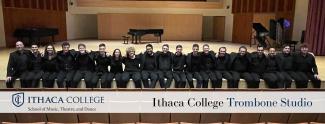 Musicians sitting across a stage wearing concert black dress. Text across bottom of page reading Ithaca College Trombone Studio.