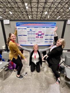Two OT Alumni and faculty standing by research poster at 2023 AOTA conference