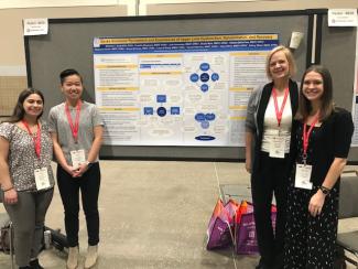 Three OT Alumni and Shannon L. Scott standing by research poster at the 2023 AOTA conference in Kansas City, KS