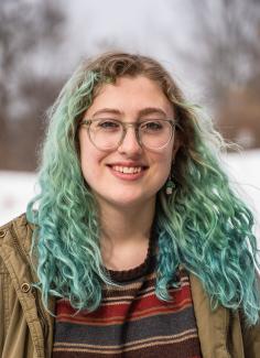 Headshot of girl with green, curly hair and glasses