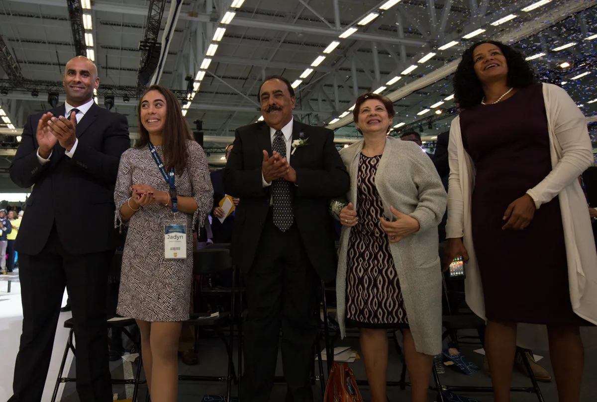 A group of five people smile and clap with confetti in the background