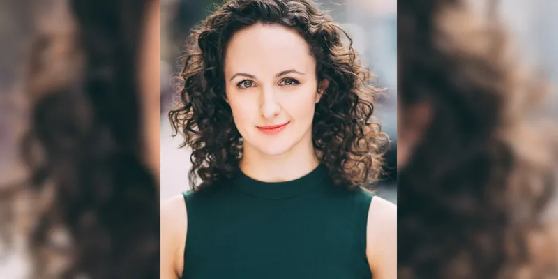 Headshot of playwright Kate Hamill, a white-skinned woman with curly brunette hair.