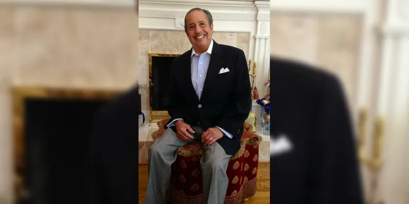 An older gentleman poses for a photo in a suit, button-down shirt, and slacks. 