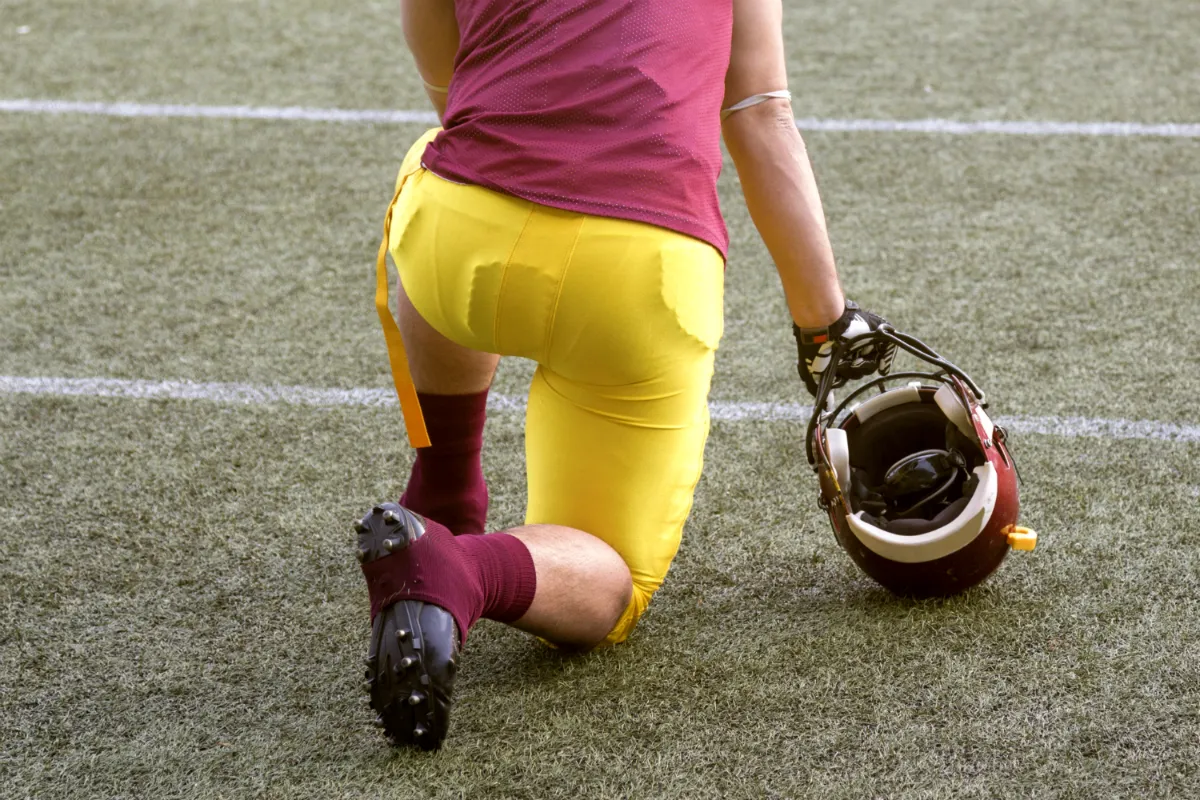 A football player in yellow and red kneels on the field