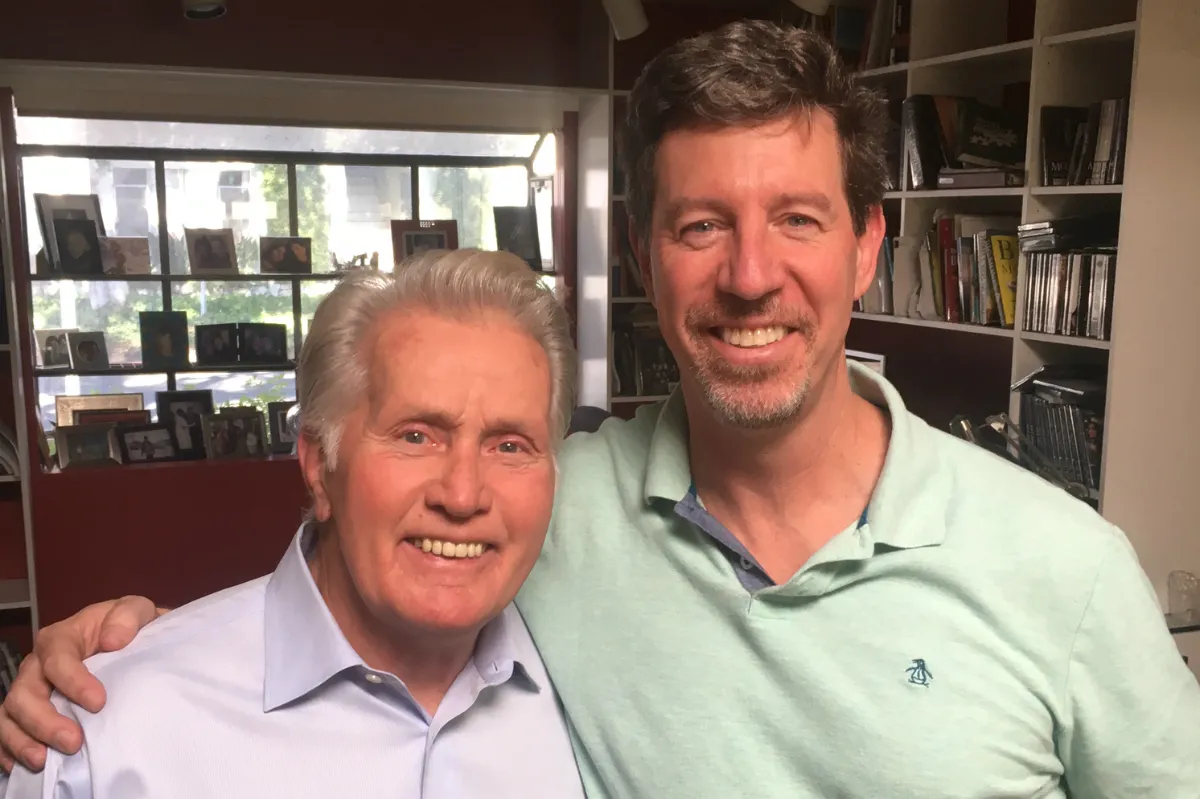 Two men stand arm in arm