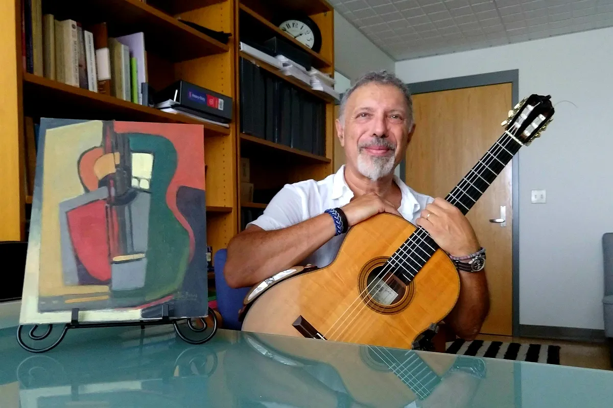 A man posing with a guitar and an abstract painting