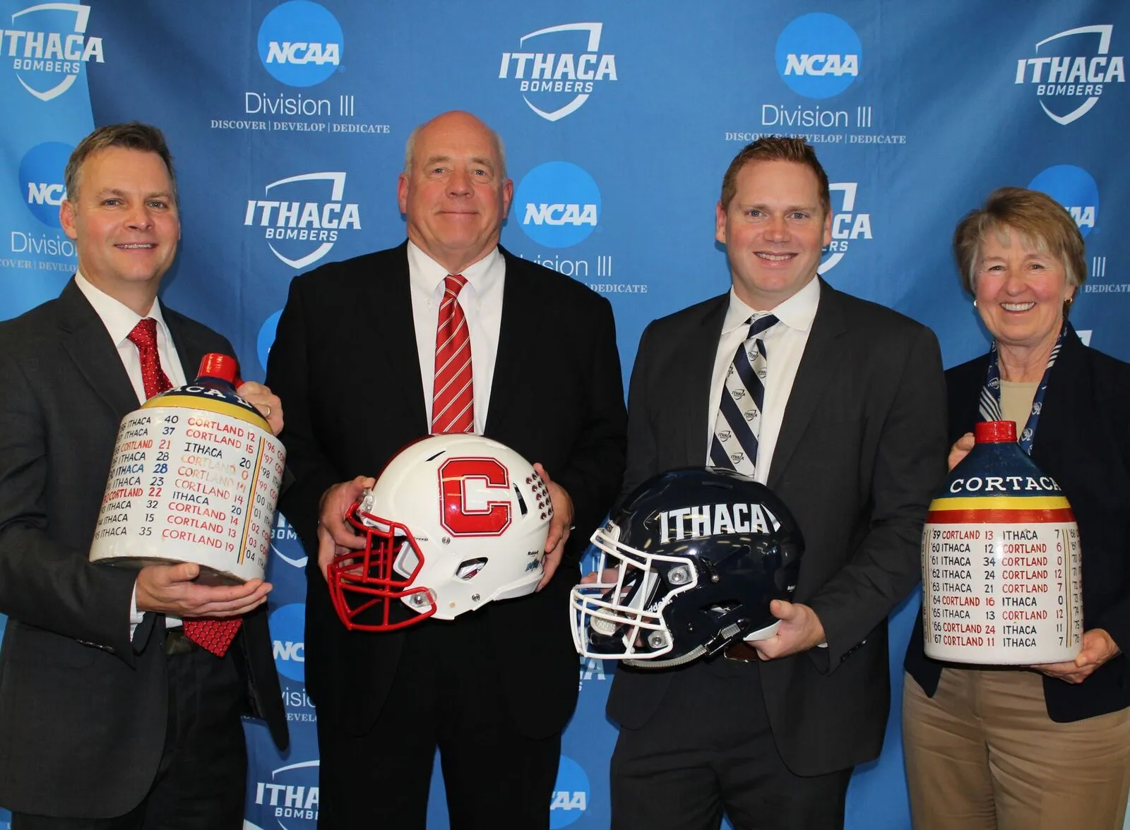 Athletic directors and football coaches from SUNY Cortland and Ithaca College holding the Cortaca jugs and football helmets