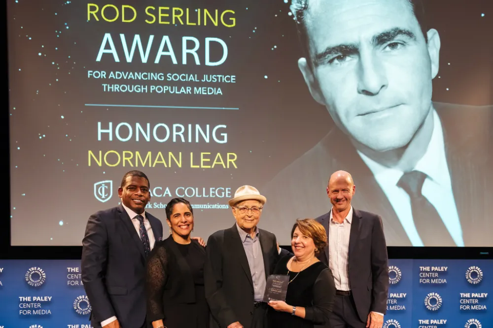 A group of men and women standing in front of a screen on stage