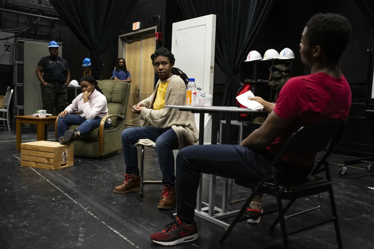 Actors dressed as auto workers sitting and standing