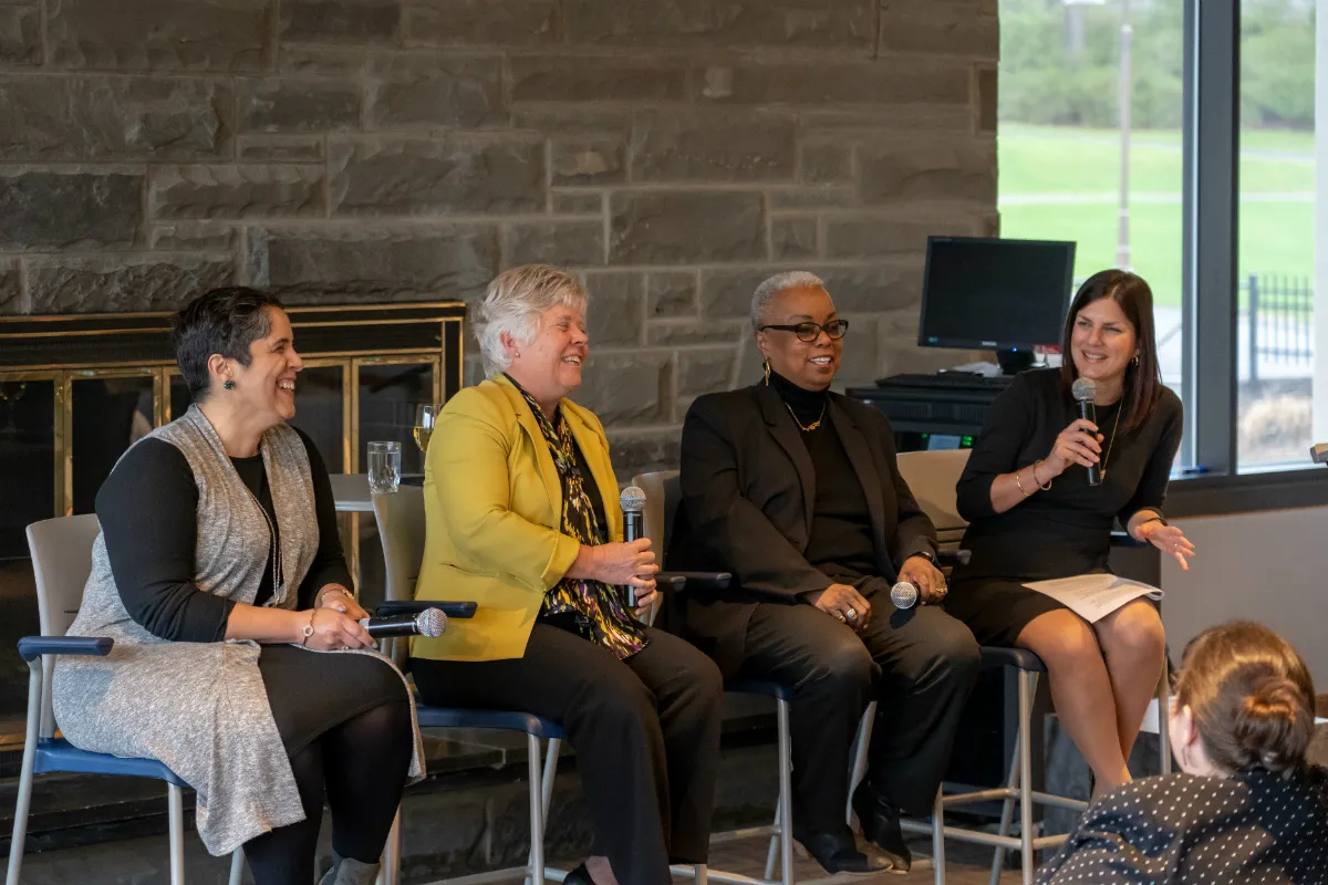 Four women speaking in front of a fireplace