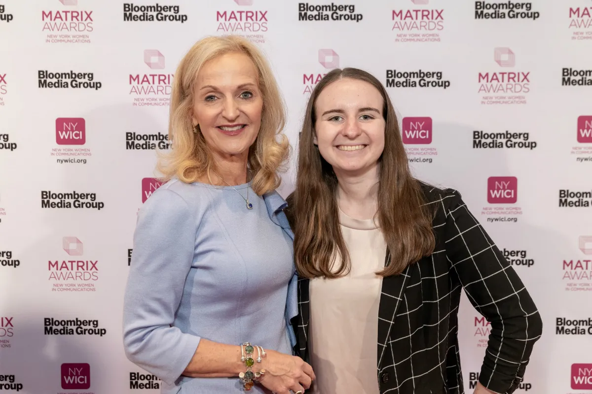 Two women pose in front of a backdrop