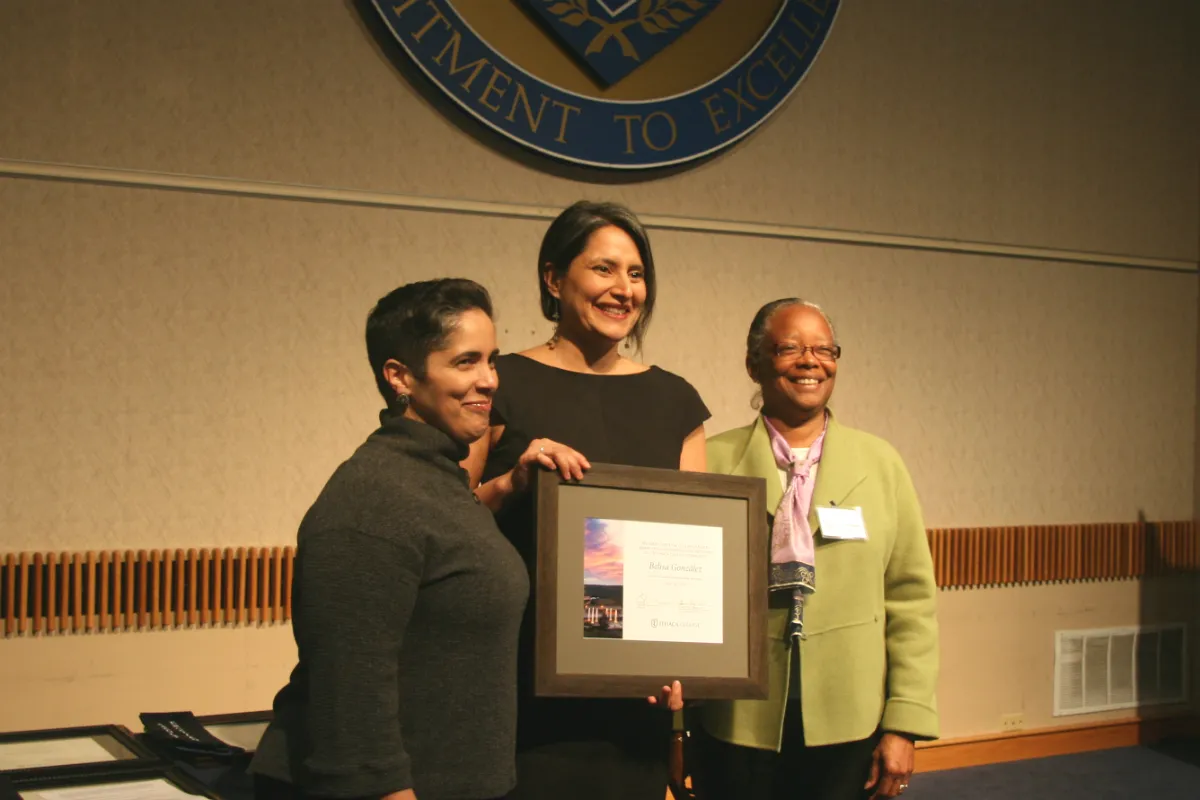Three women posing with a plaque