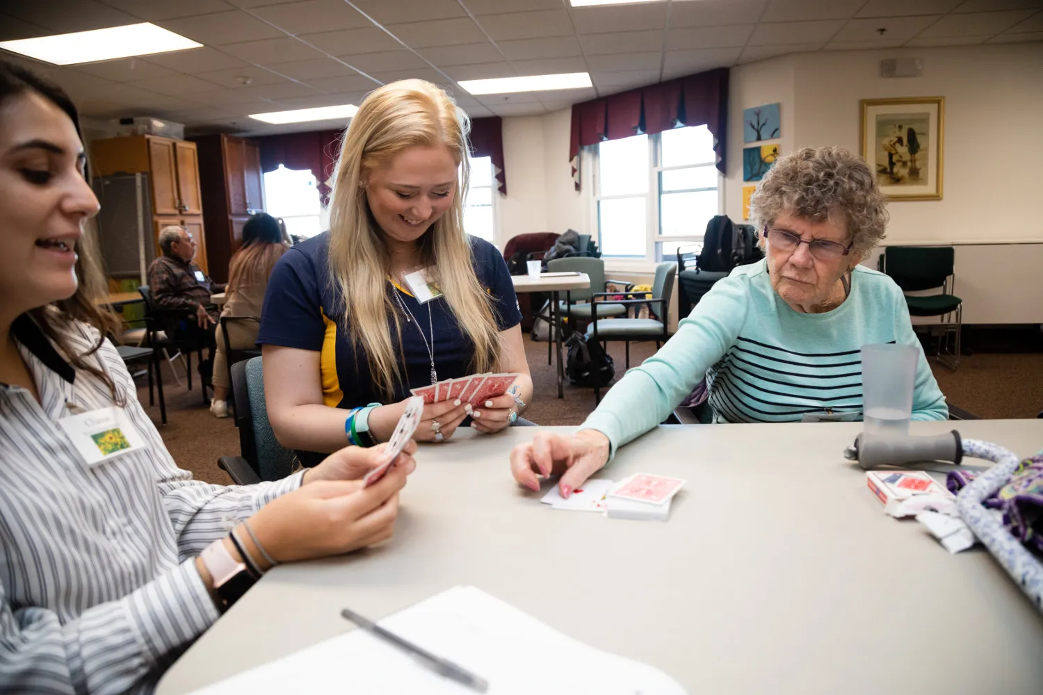Two students and one elderly participant are seating at a table playing cards.