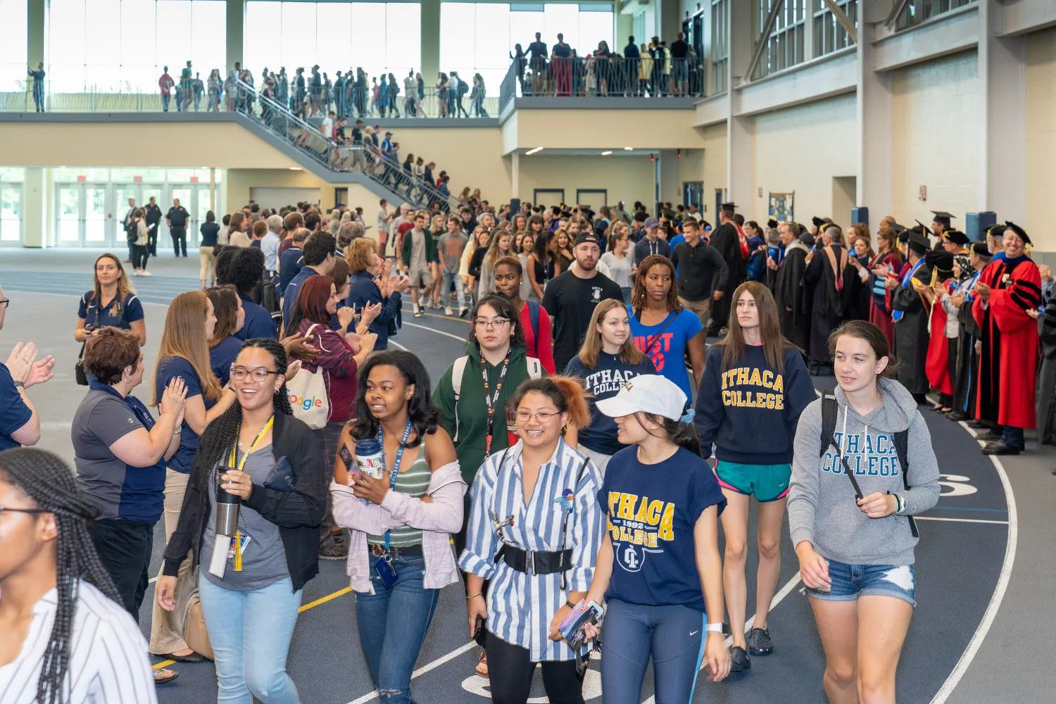 Young people walking on an indoor track with faculty cheering