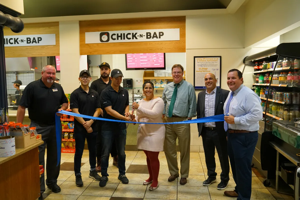 People standing in a food court with a ribbon and large scissors