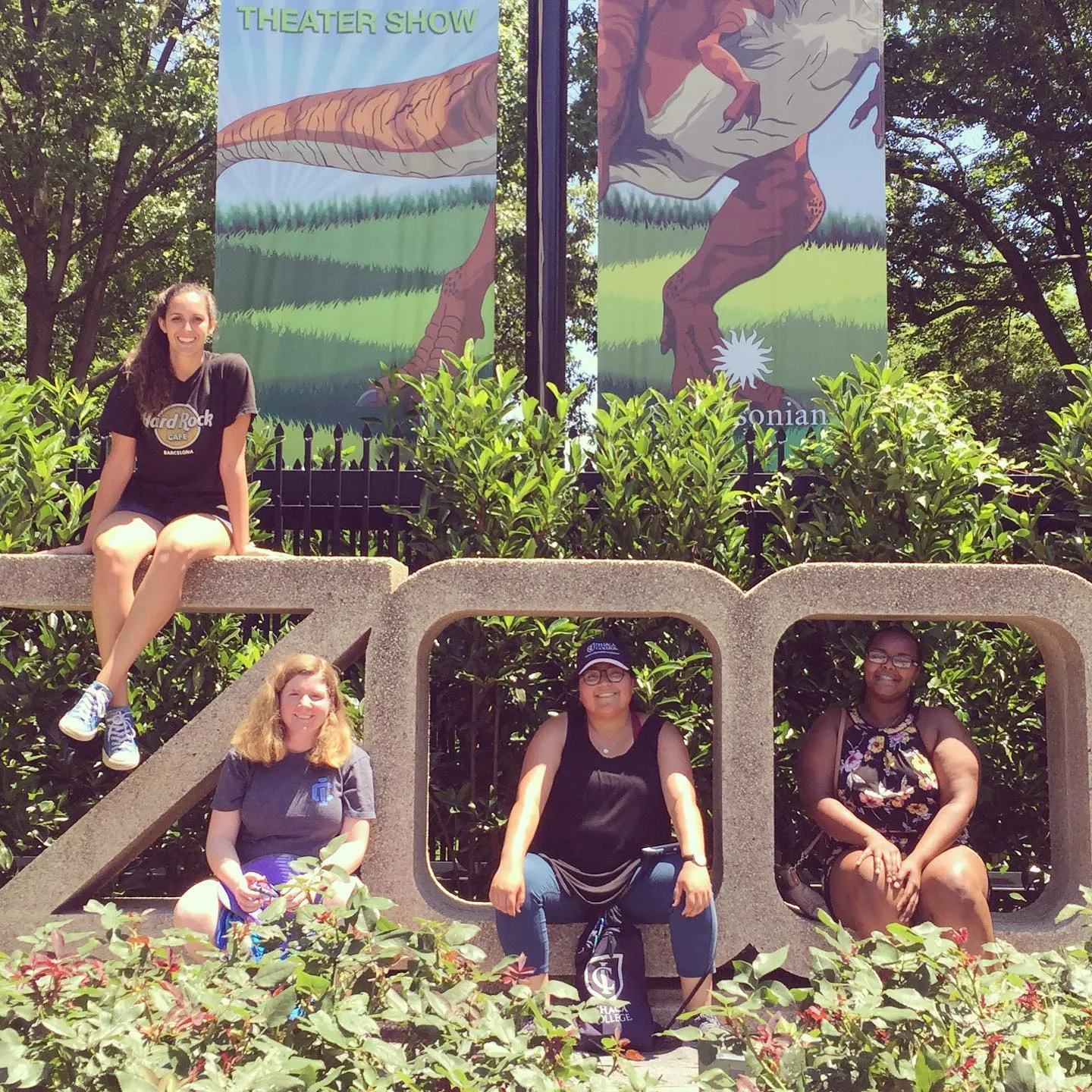 four women sit on a large concrete sculpture that says ZOO