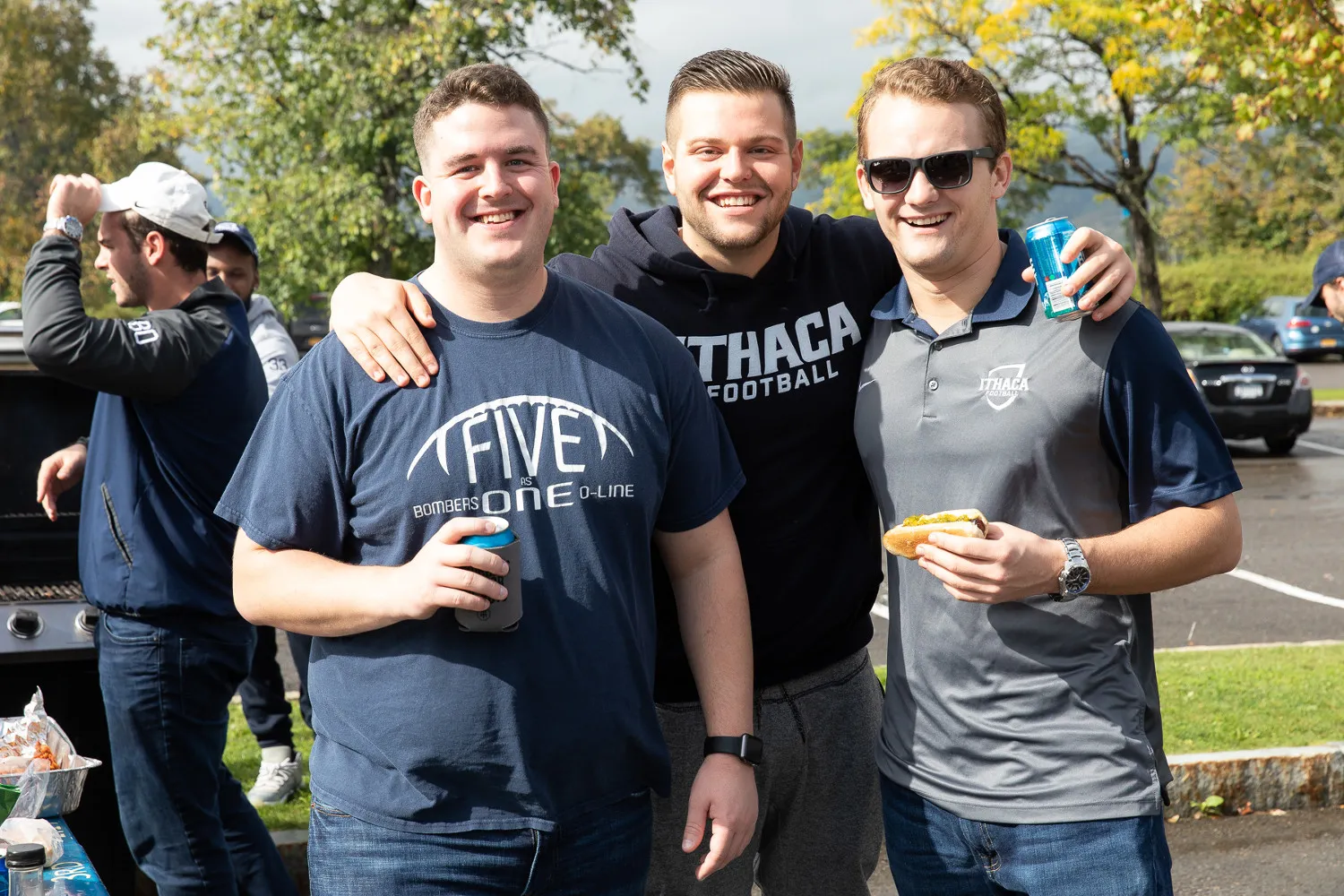 Three young men posing for a photo by a grill