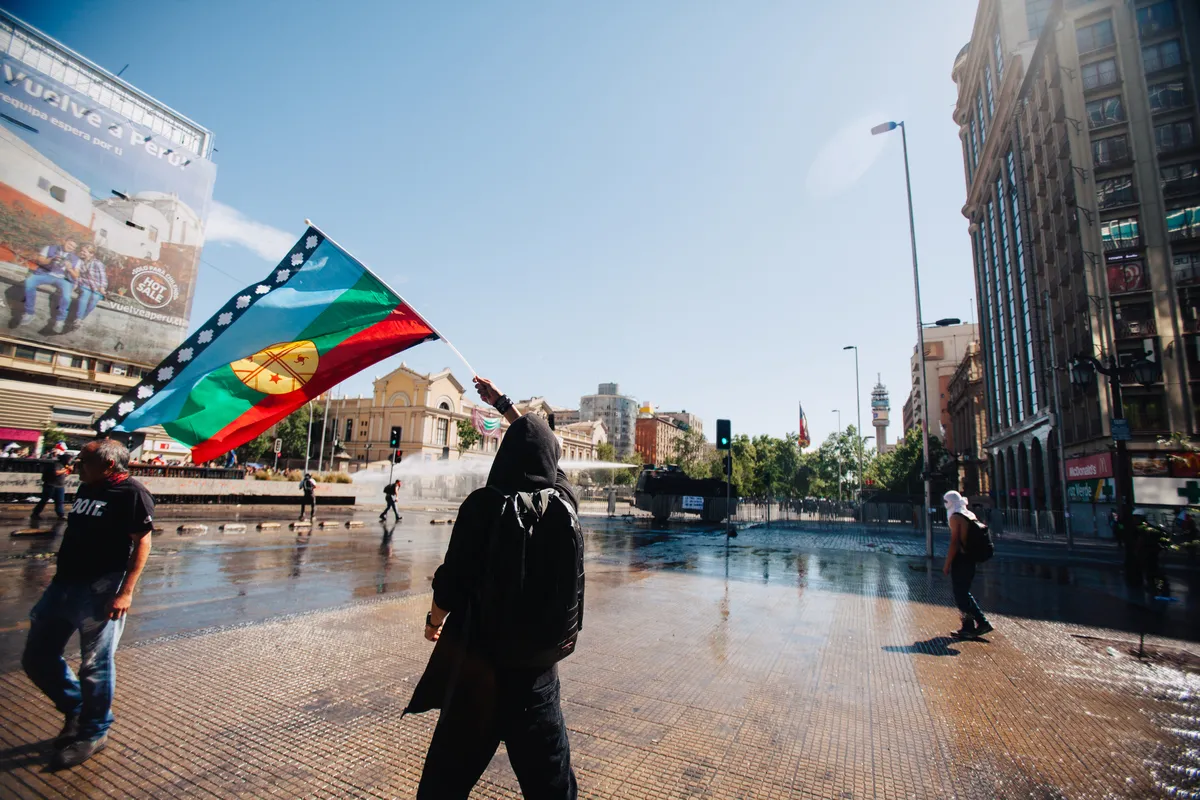 A blue, green, red and yellow flag being waved by a person in a public square