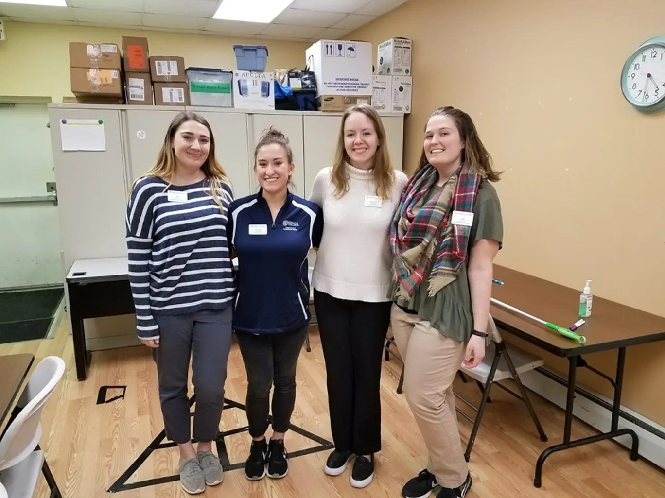 Four students are standing next to each other with their arms around one another smiling. They are at the Ithaca Free Clinic.