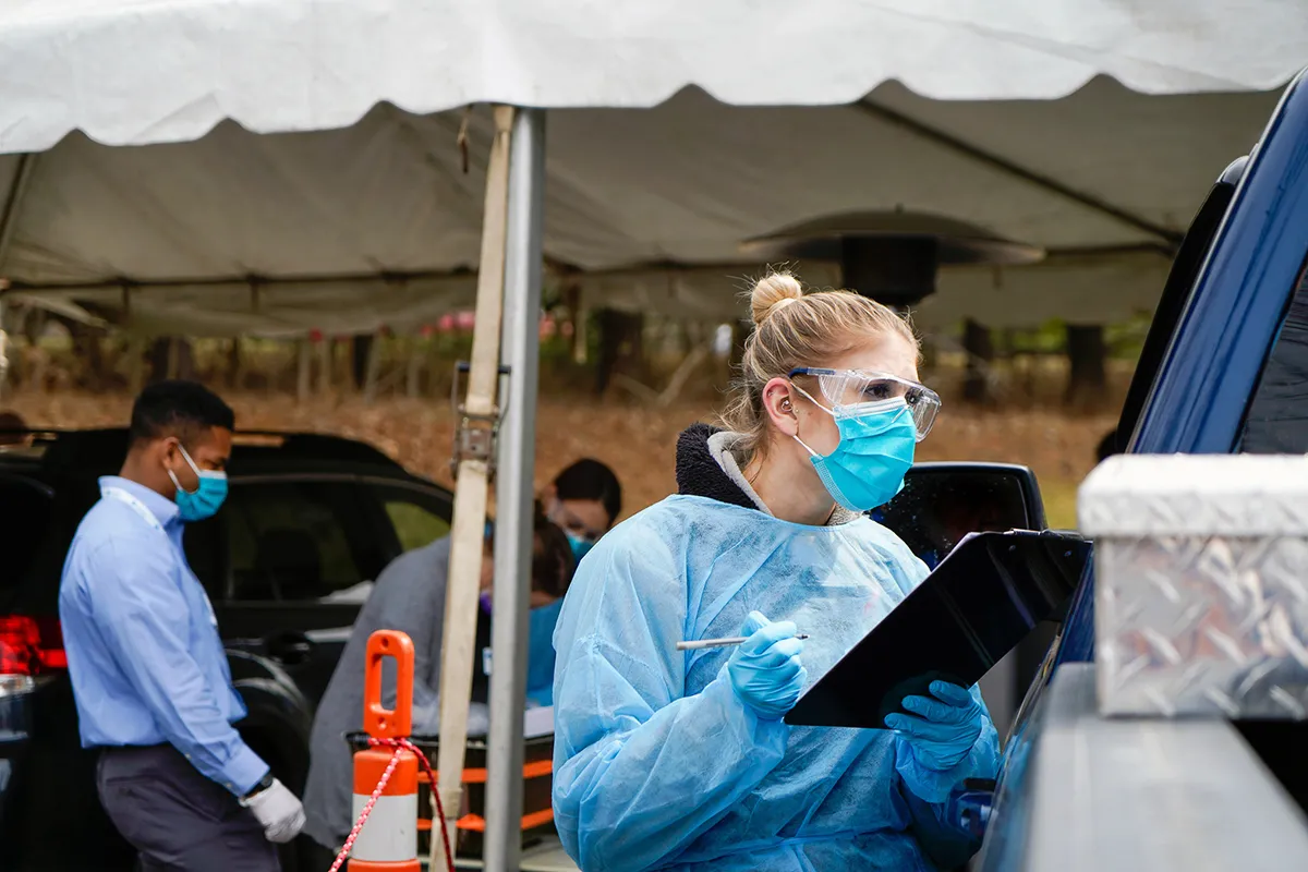 woman wearing mask and gown, talking to patient in truck