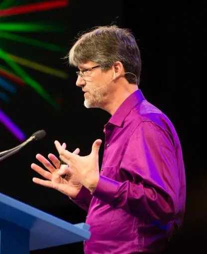Professor Luke Keller speaking at a podium with laster beams in the background.