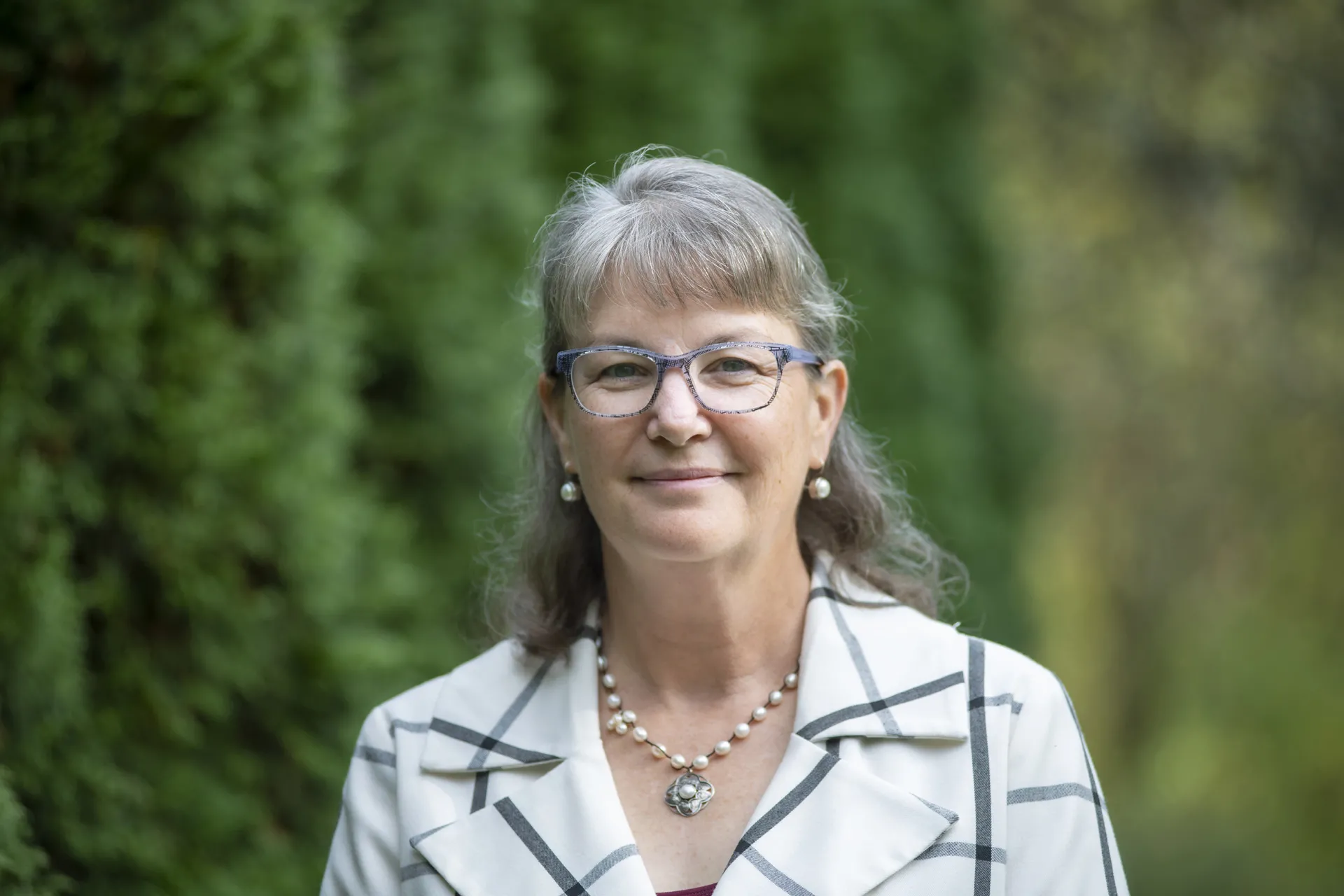 Picture of Prof. Shackell in white blazer with trees behind.