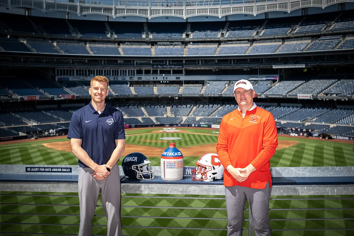 Ithaca and Cortland football coaches standing with helmets and the Cortaca Jug in the middle