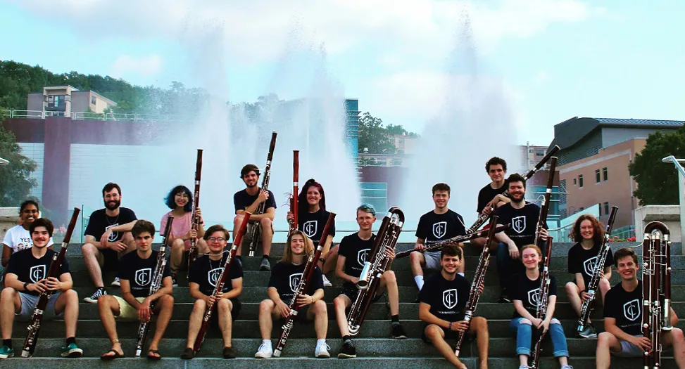Student smiling while sitting on stairs holding bassoons with fountains in the background