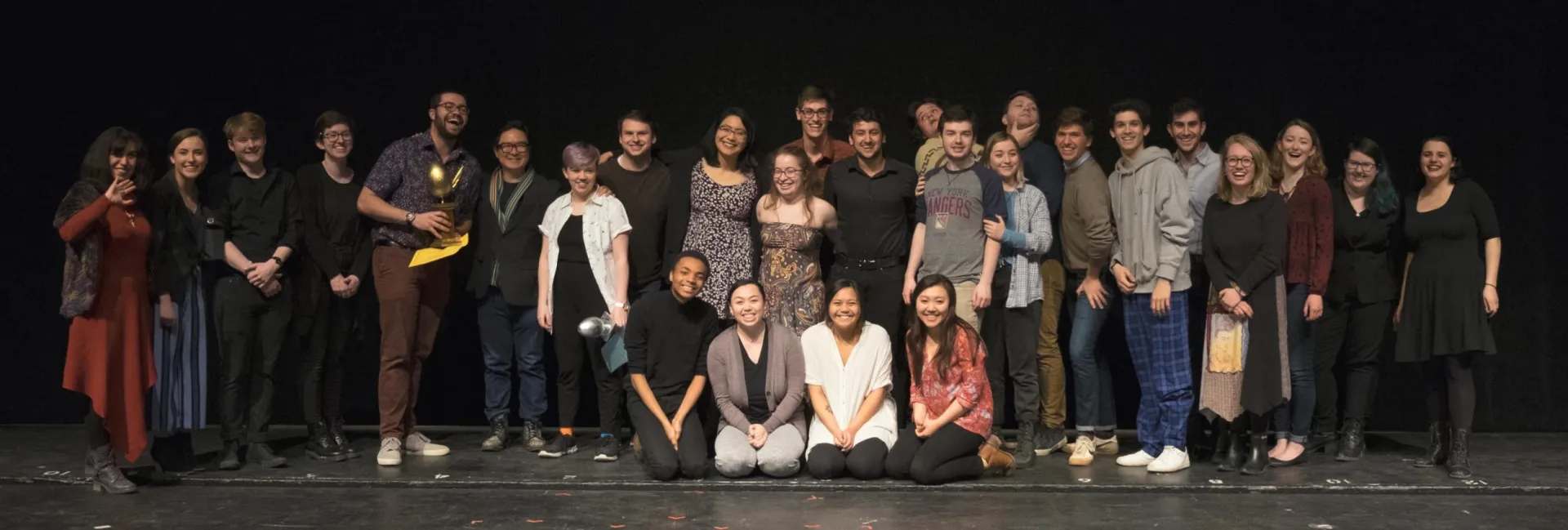 Theatre Studies students posing on a stage in front of a black curtain.