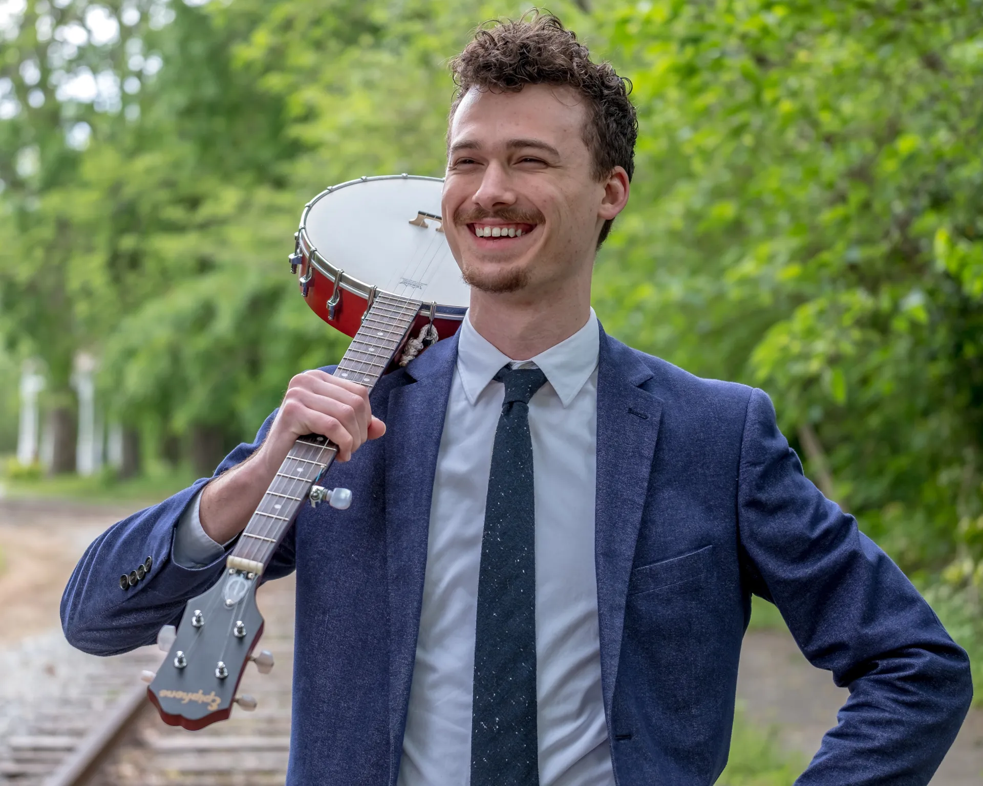 Man in blue jacket smiling with banjo rested on his right shoulder
