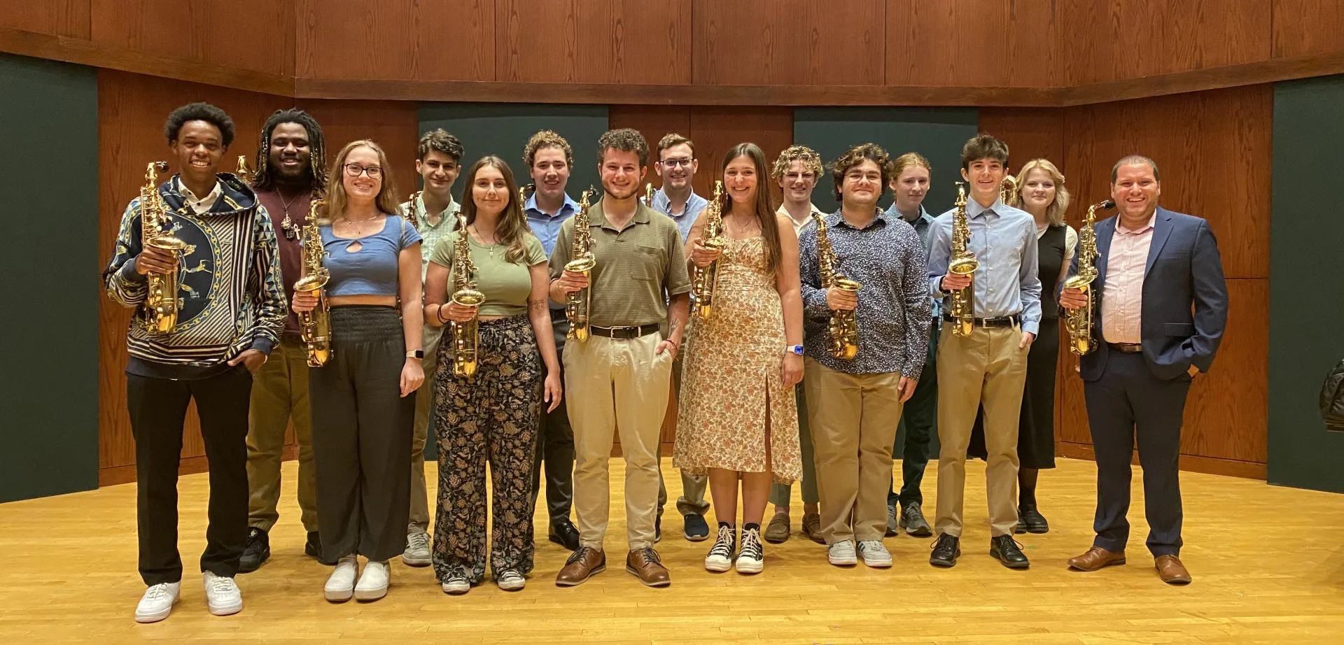A diverse array of students holding saxophones and smiling on stage.