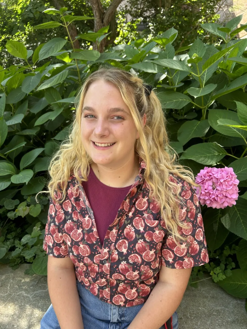 Person smiling in front of bush, sitting