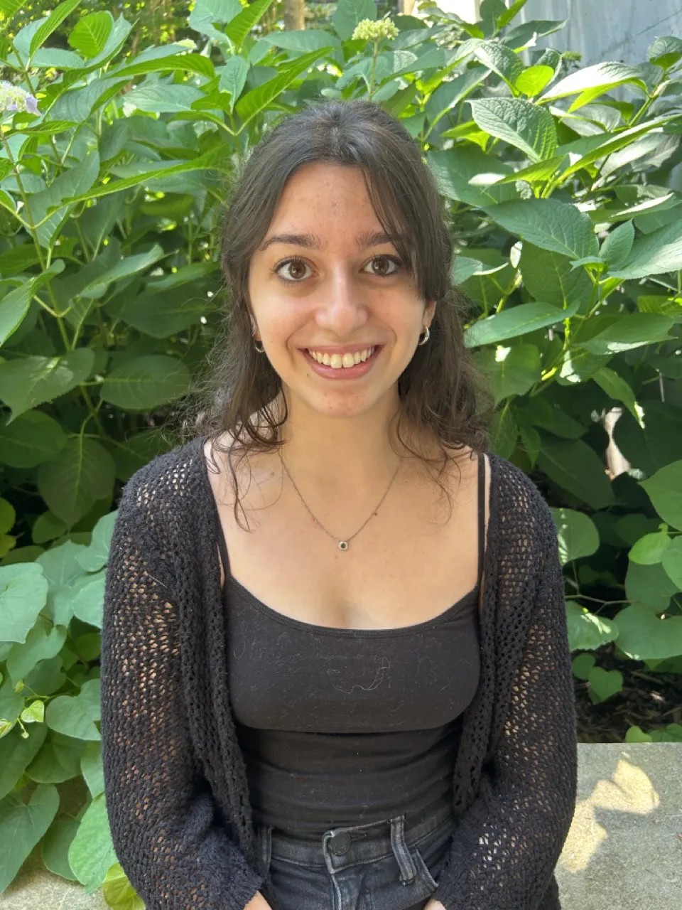 Person sitting in front of green bush smiling