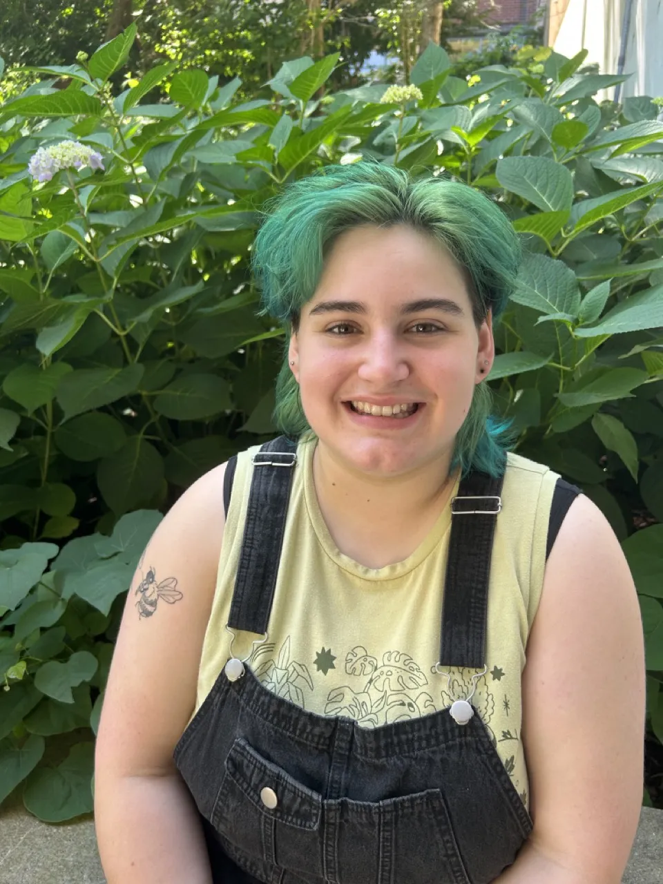 Person sitting in front of green bush smiling