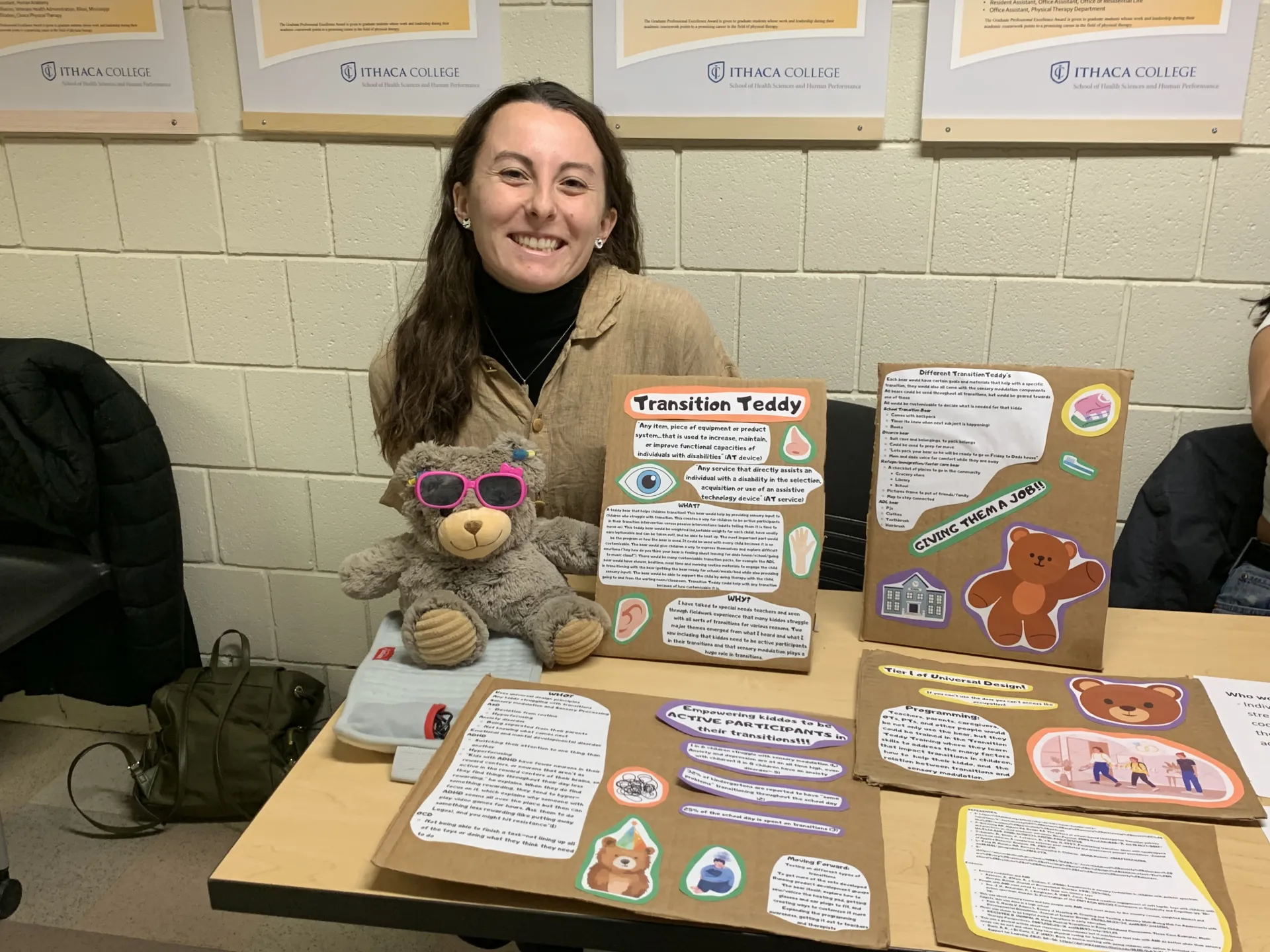 A person sitting at a table with a teddy bear to help transitioning to different classes