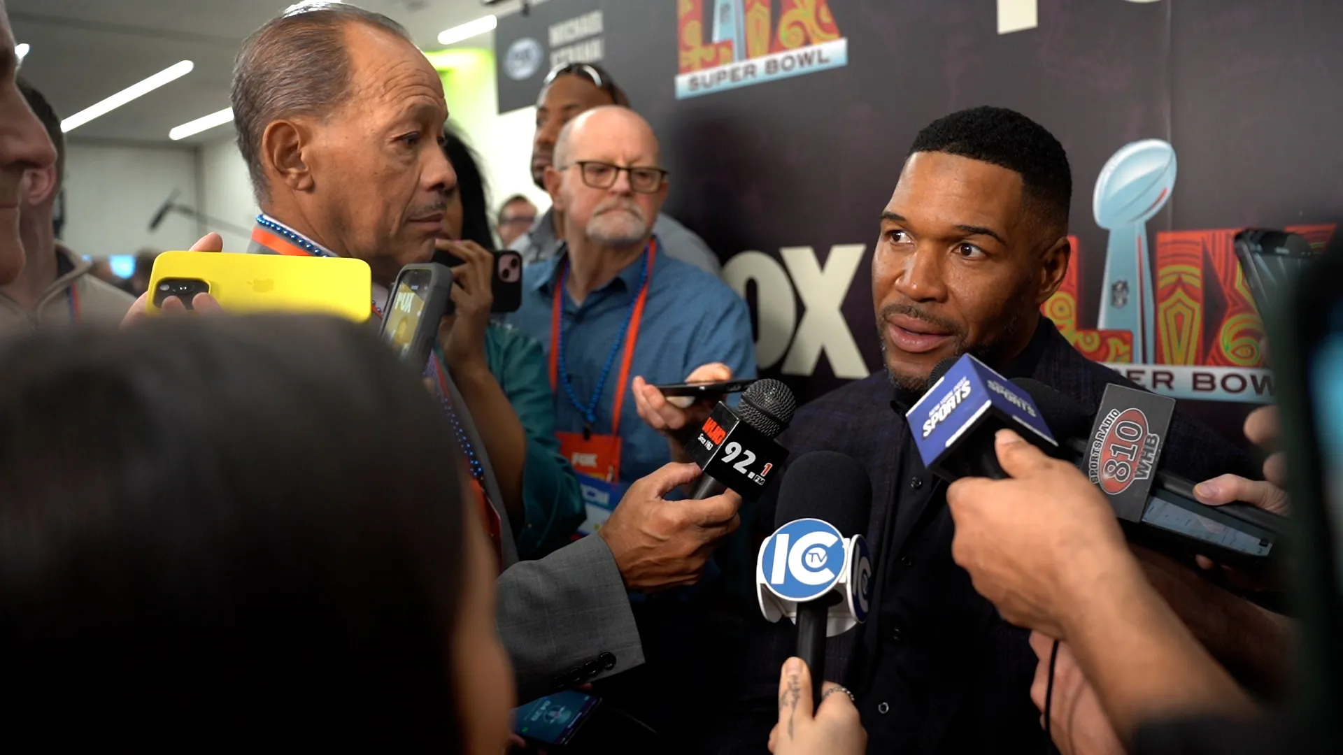 Reporters with microphones interview NFL legend and analyst Michael Strahan.