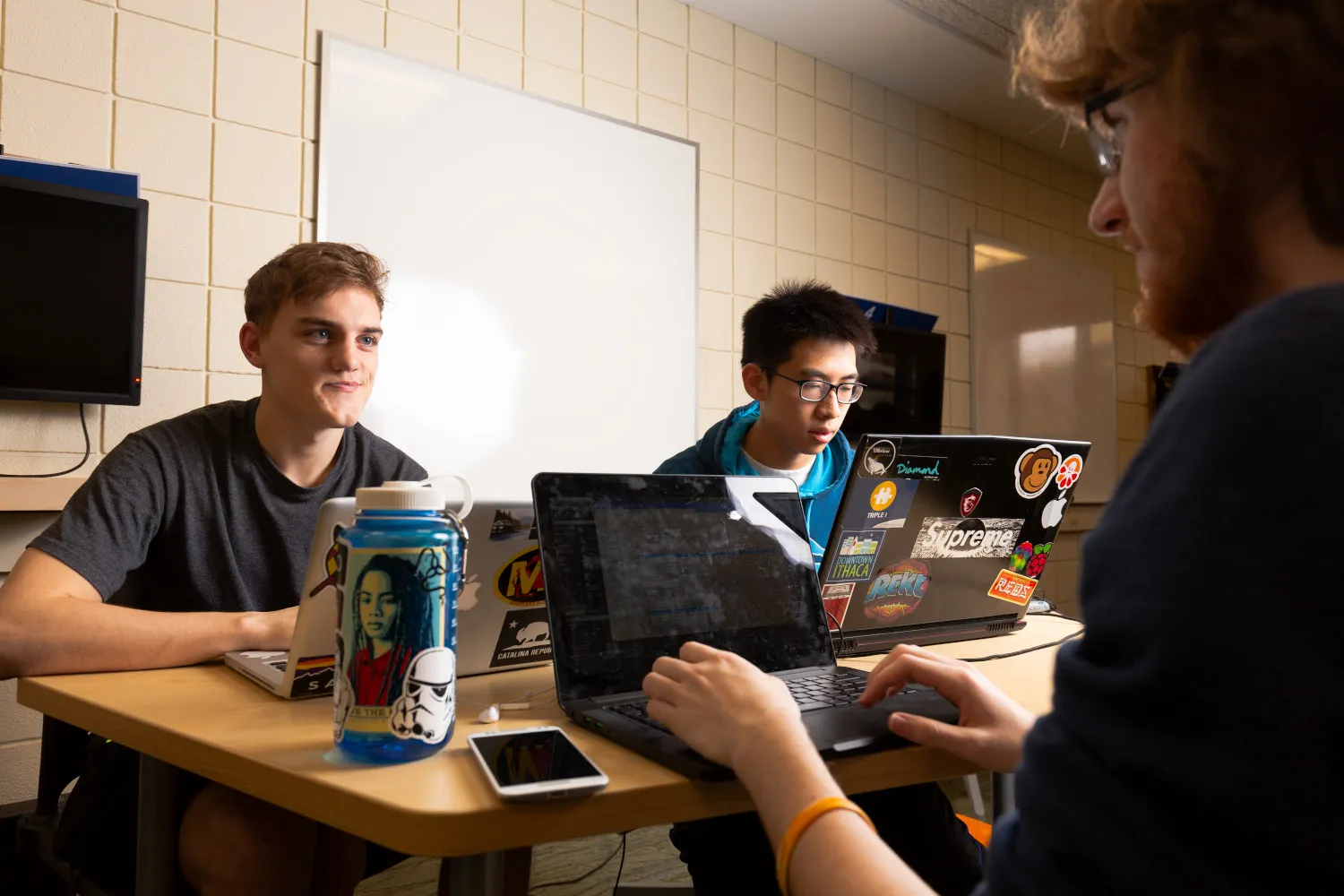 a group of three male students sitting at a table working on laptops