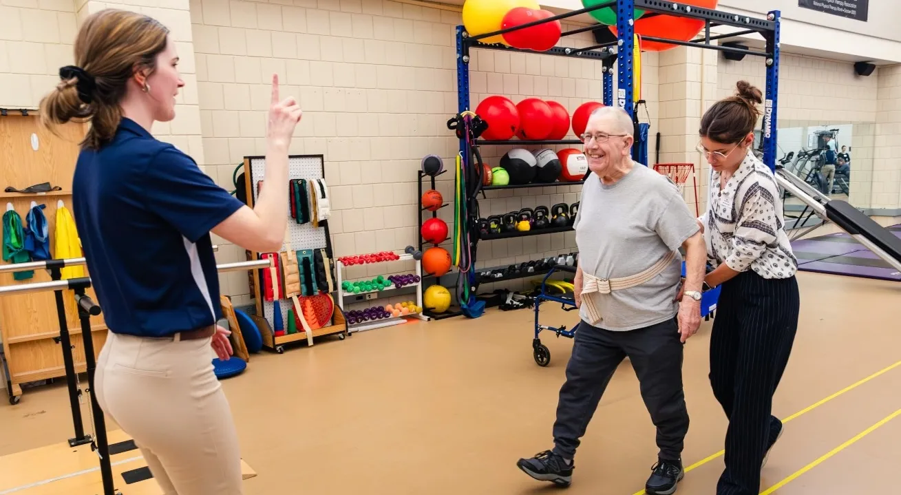 two students work on a walking exercise with an elderly patient