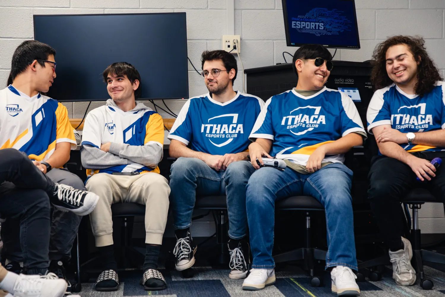 A group of five students wearing IC Esports Jerseys talk amongst themselves in a classroom.