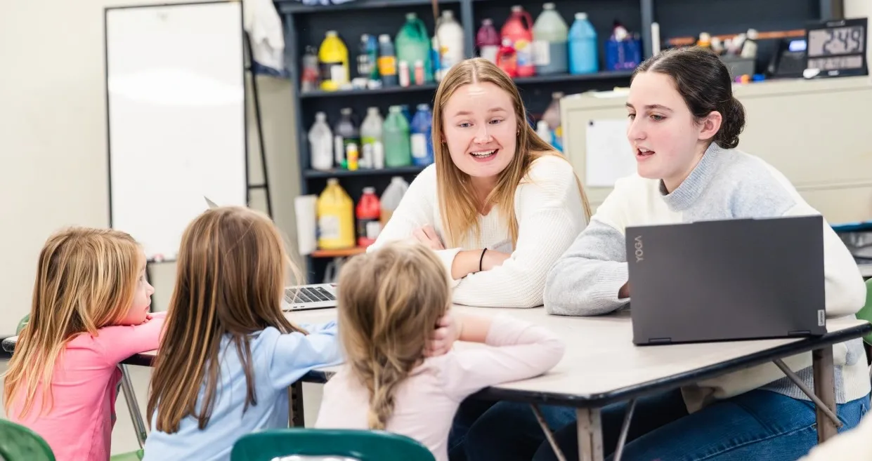 Two female Ithaca College students talk with a group of three elementary students. 