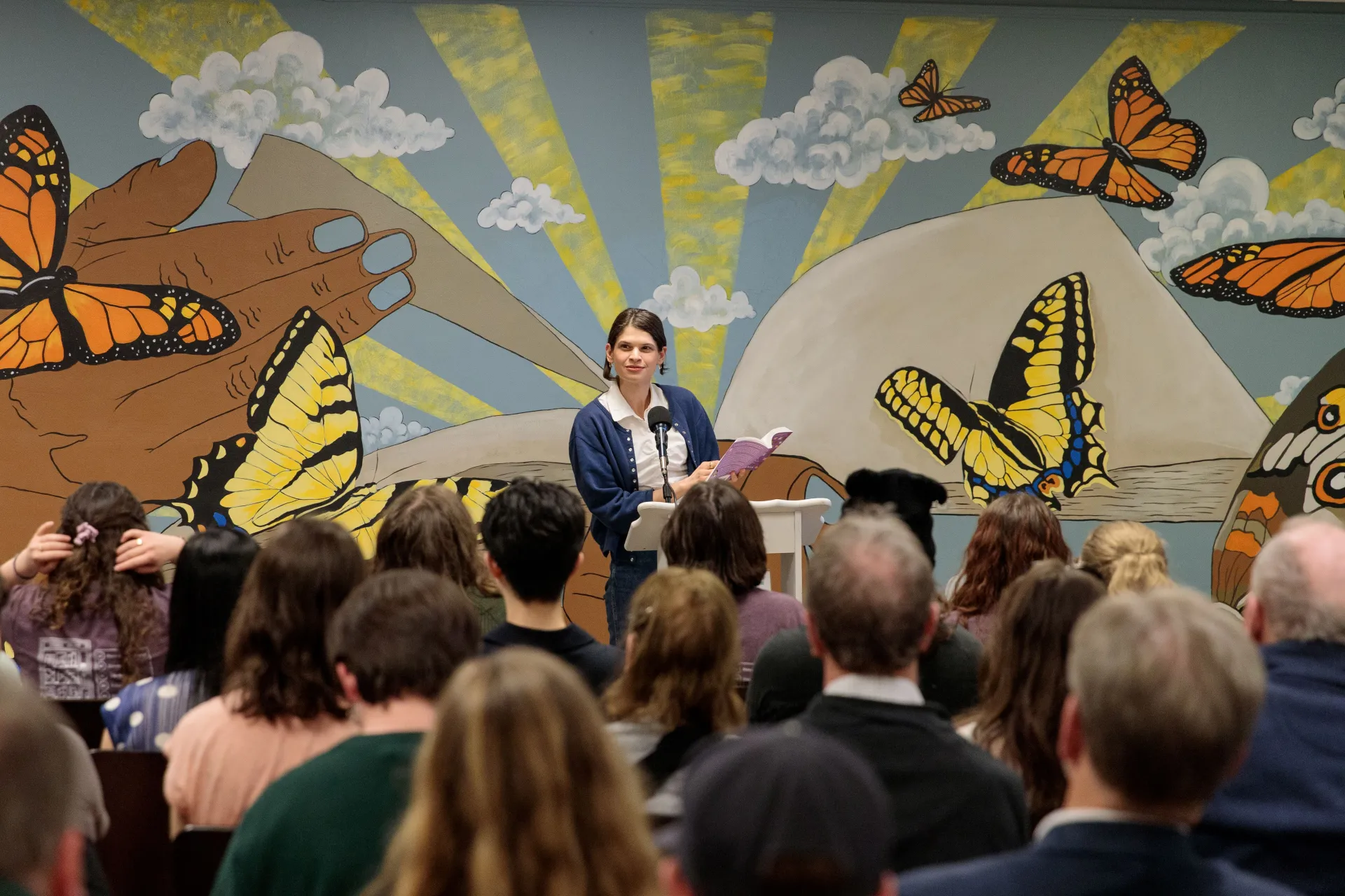 An author reads from a podium in a packed venue. 