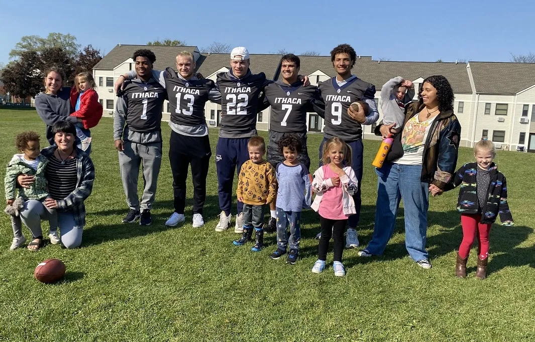 students wearing football jerseys pose outside with several moms and their children