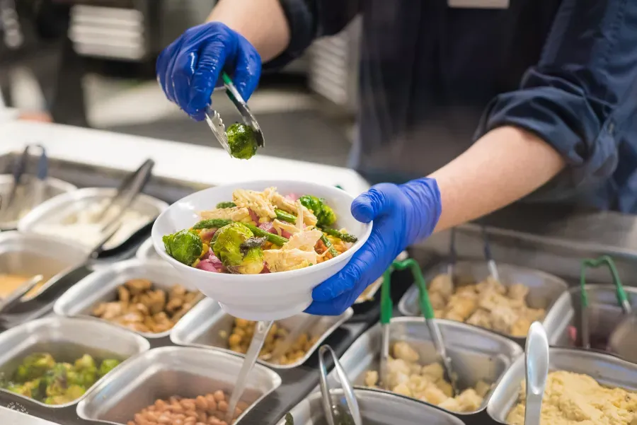 A campus dining staff member builds a salad. 