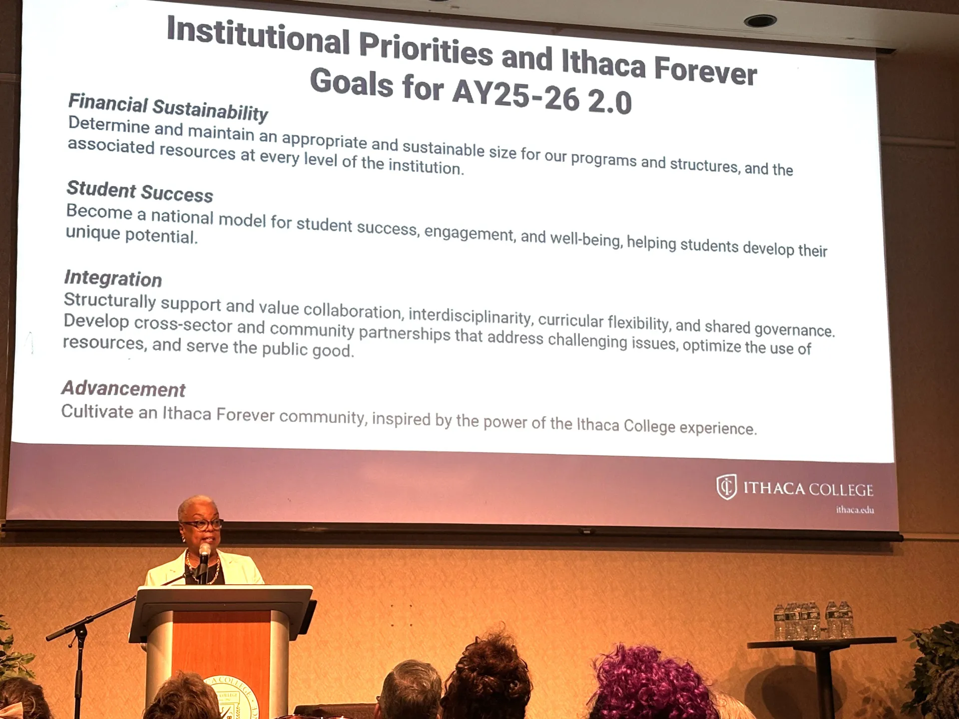 woman standing at podium with text on screen behind her