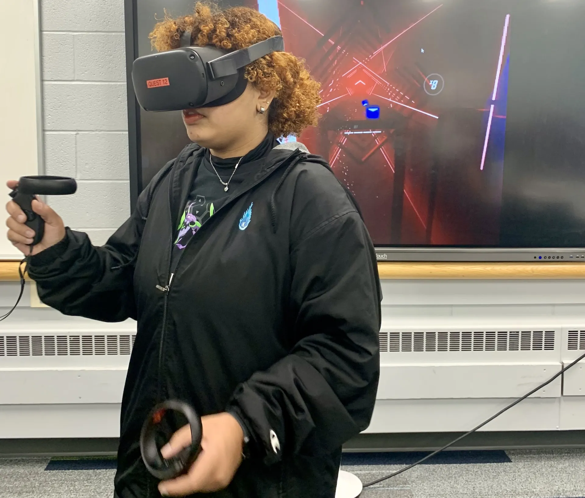 Person standing with virtual reality headset on and a screen is behind them.
